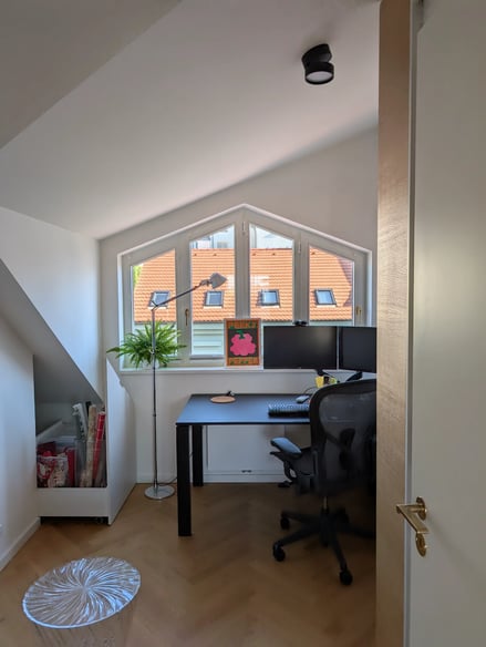 Moderní pracovna s oknem, stolem a židlí.